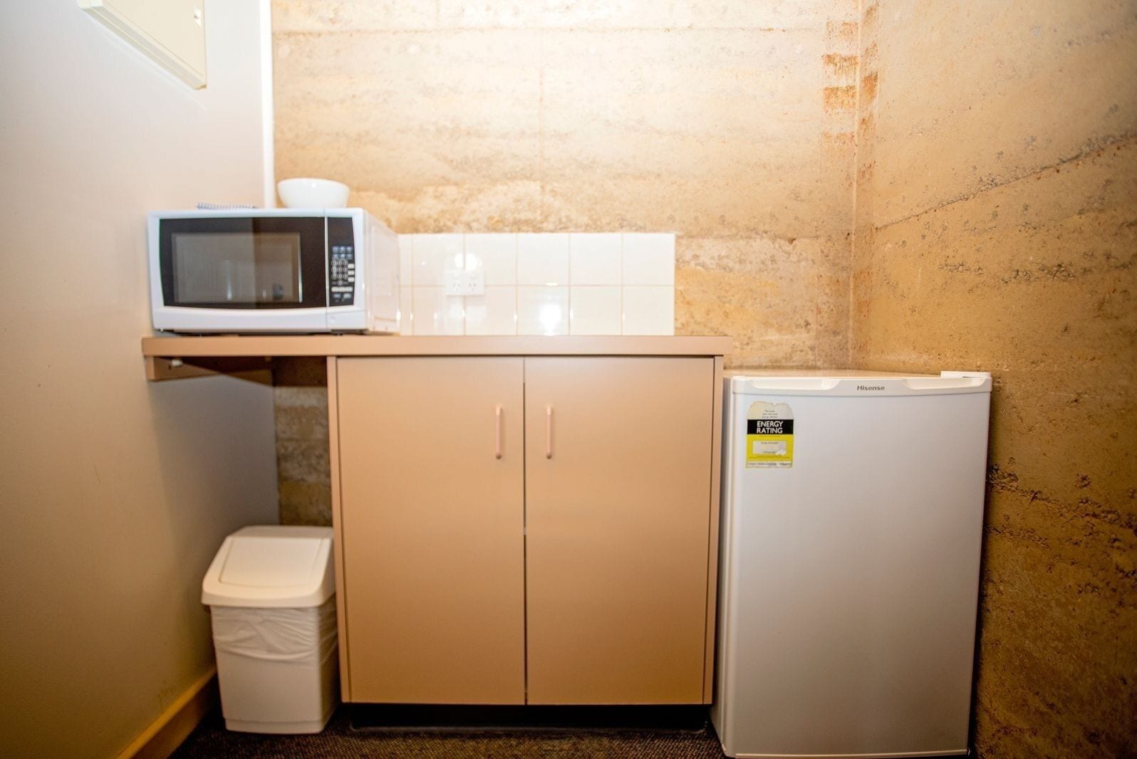 Een compacte kitchenette met een magnetron, een kleine koelkast en een vuilnisbak.