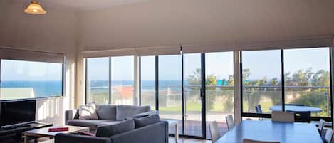 Amplia sala de estar con un televisor grande, sofá gris y una mesa de comedor con sillas.