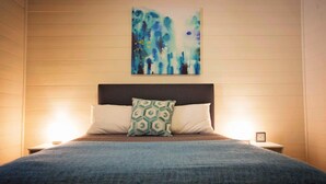 Une chambre à coucher comprenant un lit, deux tables de chevet, une commode et un tableau accroché au mur.