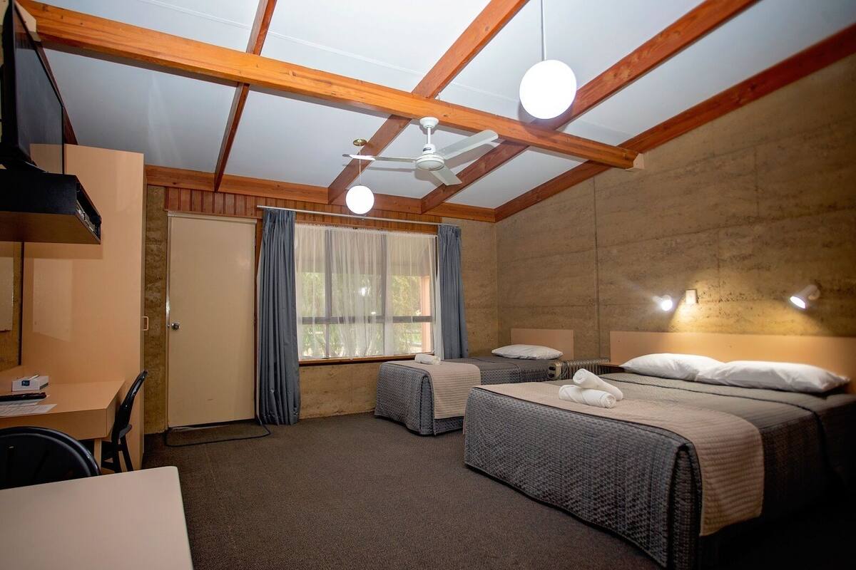 Une chambre avec deux lits, un bureau et une fenêtre avec des rideaux.