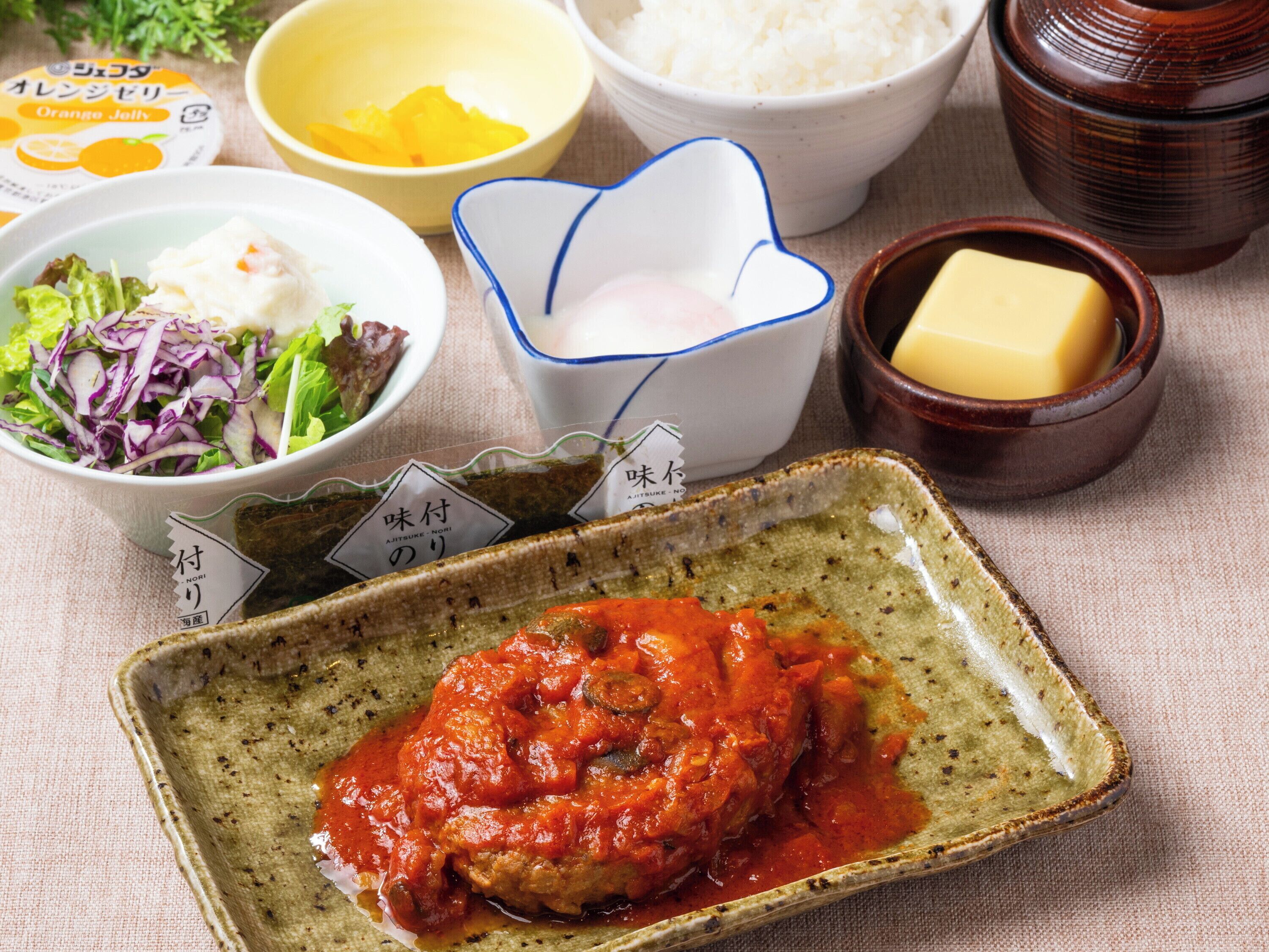 Una comida con varios platos, incluyendo un guiso de carne con tomate, una ensalada, un bol de arroz y una porción de mantequilla.