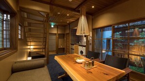 A traditional Japanese-style room with a wooden dining table, chairs, and a large window with a view of greenery.