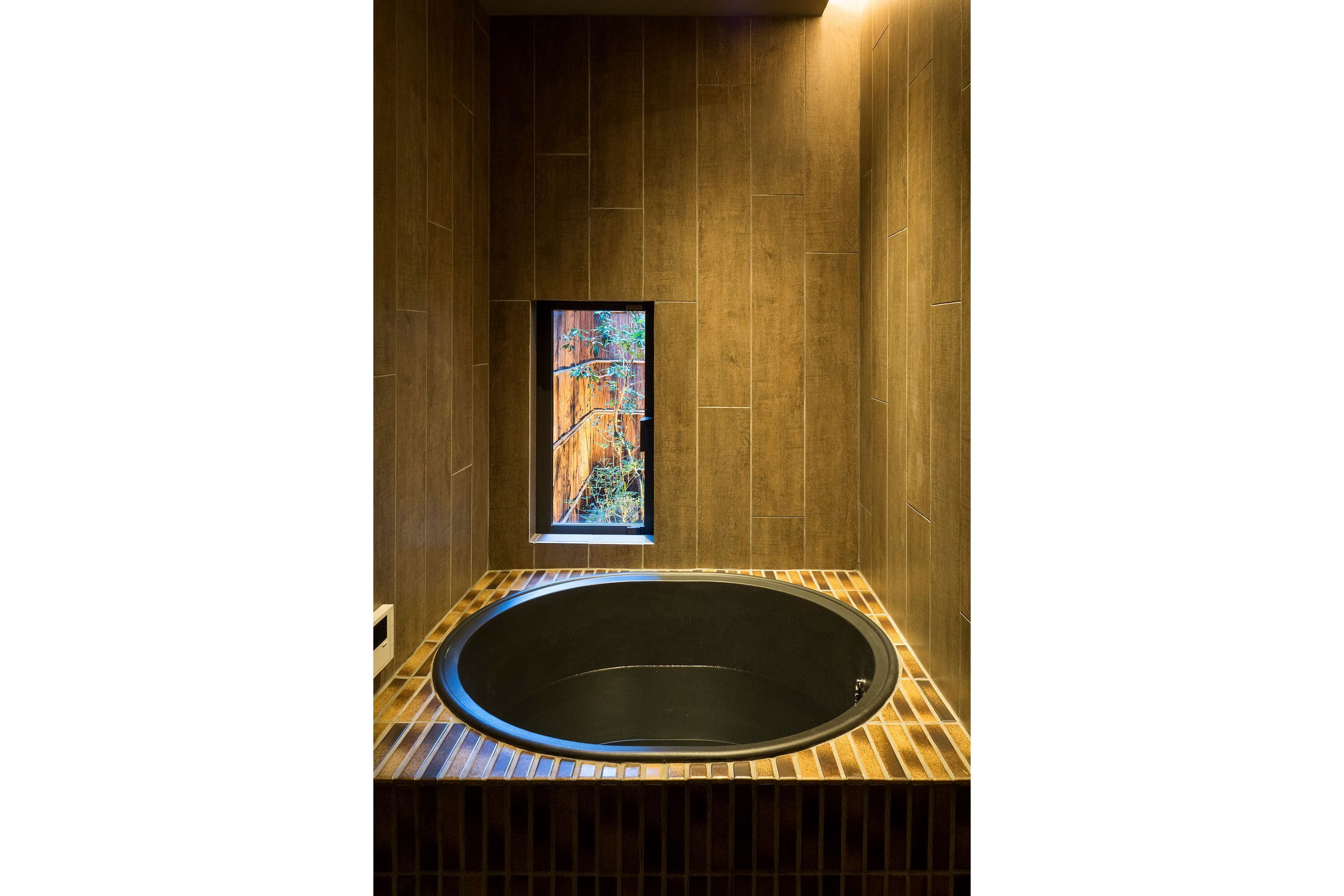 A modern bathroom with a freestanding bathtub, wooden paneling, and a small window with a view.