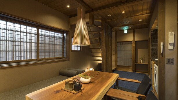 A wooden dining table with a bench, a hanging light fixture, and a view of a traditional Japanese room with tatami flooring and sliding doors.
