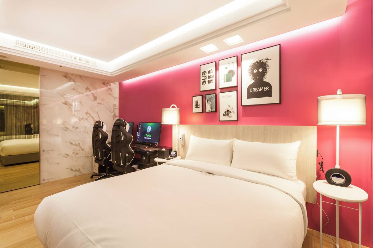 A modern hotel room with a large bed, a desk with a computer, and a TV.