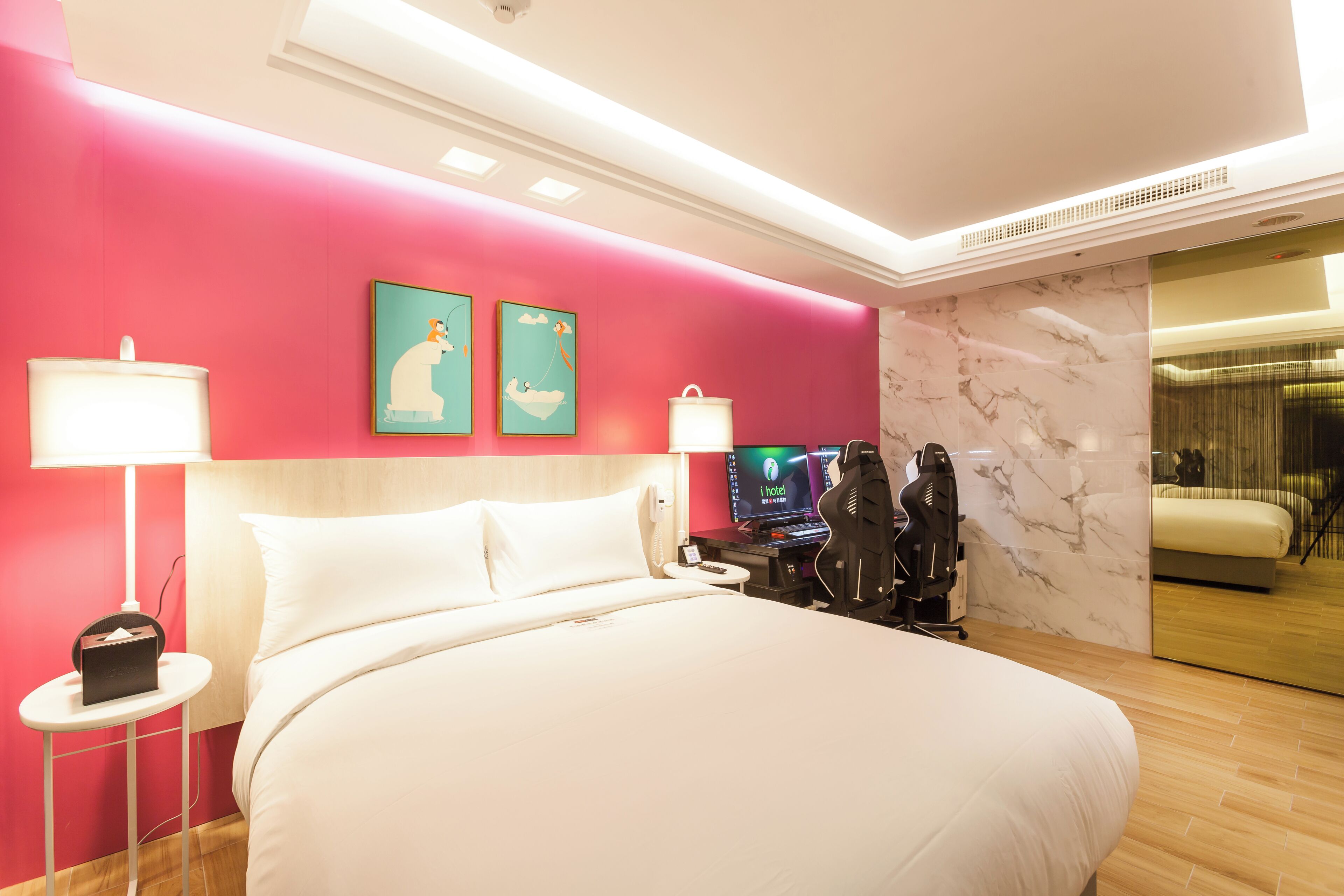 A modern hotel room with a large bed, a bedside table with a lamp, a TV, and a massage chair.