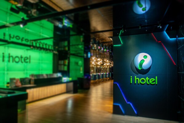 A modern hotel interior with a reception area, a bar, and a visible logo.