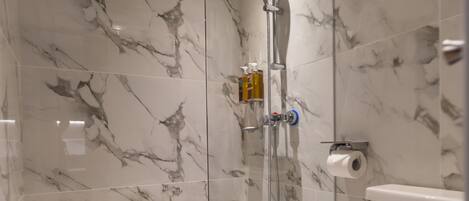A modern bathroom with a glass-enclosed shower, marble walls, and a white toilet.