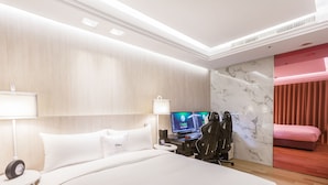 A modern hotel room with a large bed, two bedside tables, a desk with a computer, and a TV.
