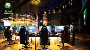 A modern gaming lounge with multiple gaming stations, ergonomic chairs, and a prominent i hotel logo.