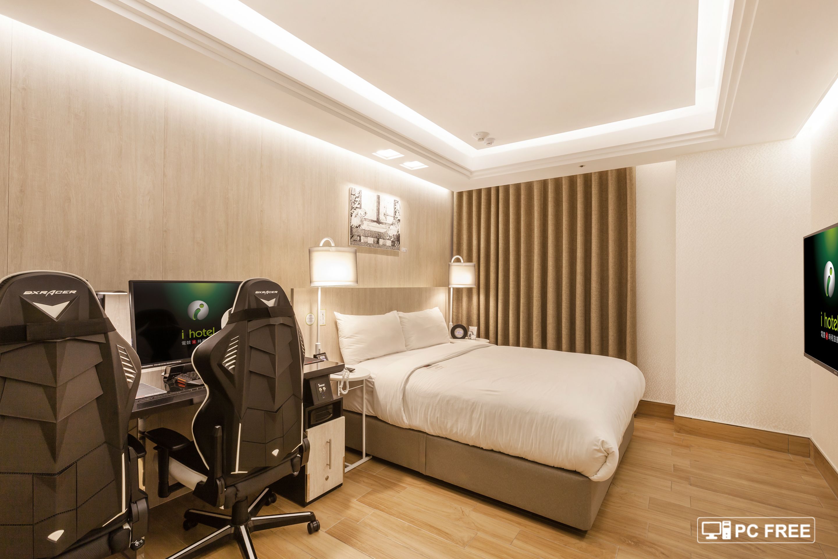 A hotel room with a bed, two desks with computers, and a TV.