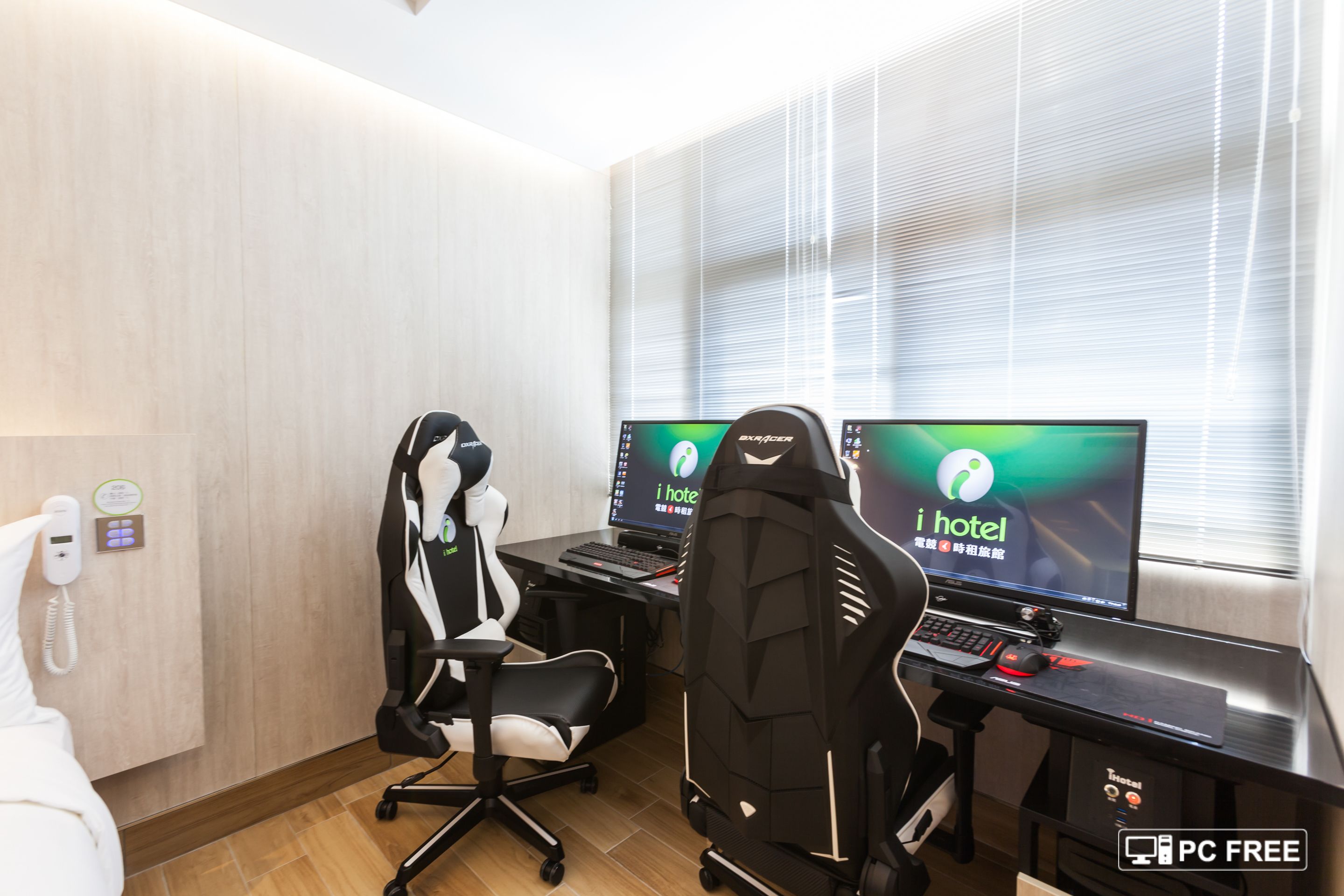A hotel room with two gaming chairs, two monitors, a desk, and a PC.