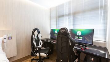 A hotel room with two gaming chairs, two monitors, a desk, and a PC.