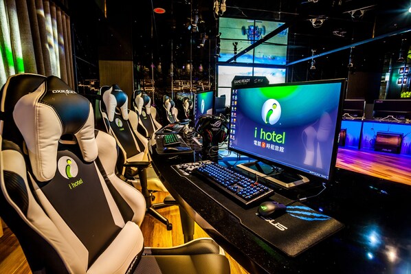 Una configuración para juegos con múltiples sillas, un monitor grande que muestra 'i hotel' y un teclado.