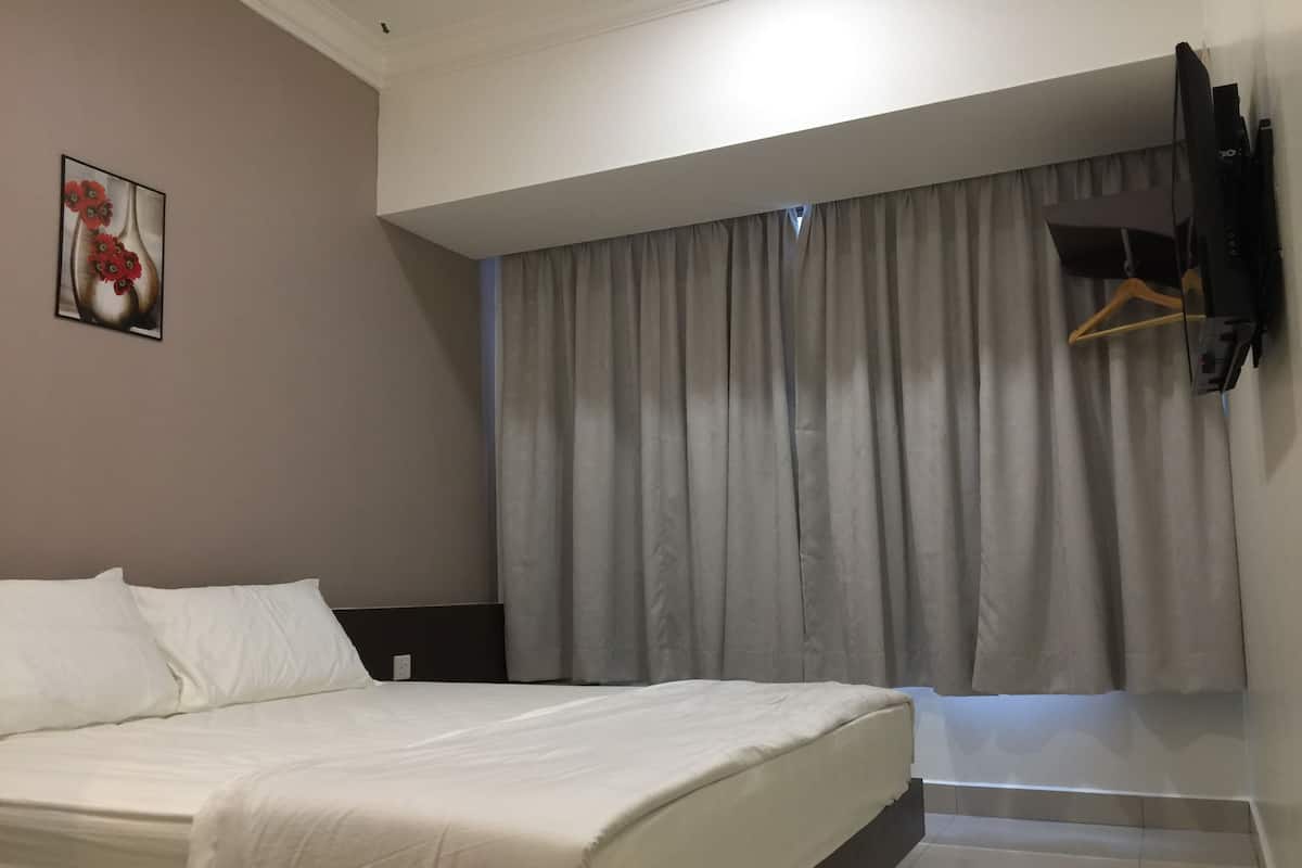 A hotel room with a bed, a flat-screen TV mounted on the wall, a window with curtains, and a small wooden hanger on the wall.
