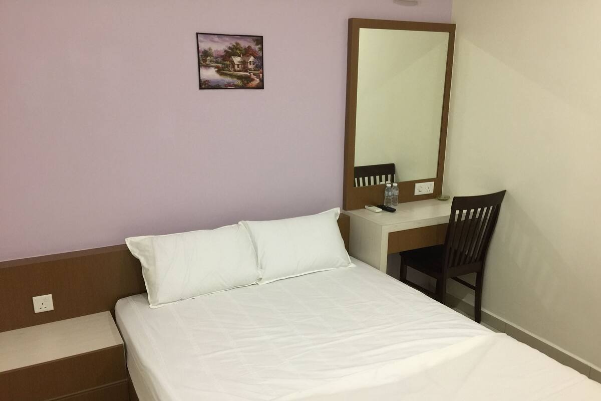 A hotel room with a bed, a desk, a chair, a mirror, and a small painting on the wall.