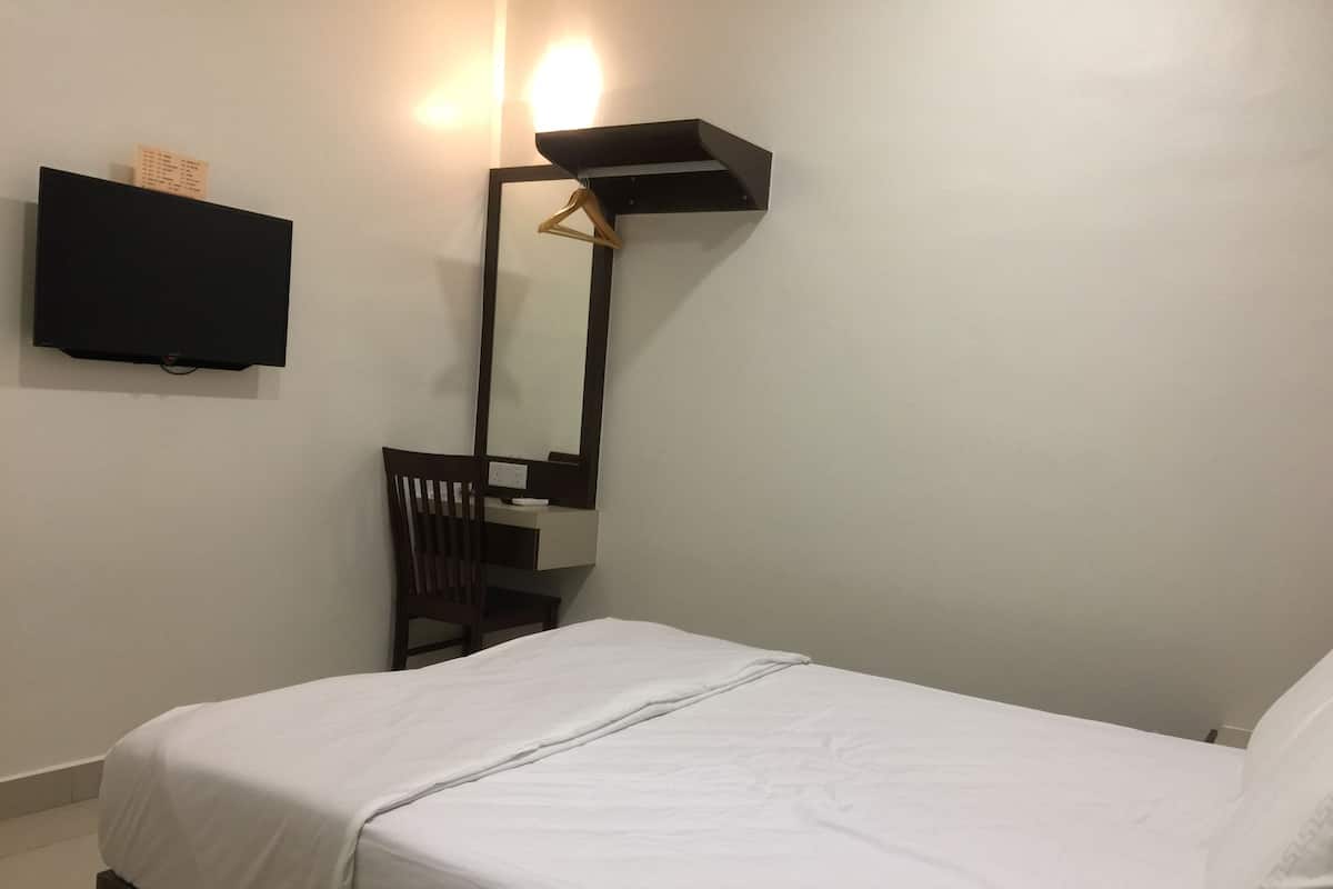 A neatly made bed with white bedding, a wooden chair, a desk with a mirror, and a flat-screen TV mounted on the wall.