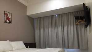 Una habitación de hotel con cama, televisor montado en la pared y ventana con cortinas.