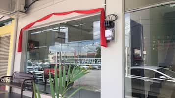 Entrada de un hotel con un toldo rojo, un banco y una puerta de cristal que refleja la vista de la calle.