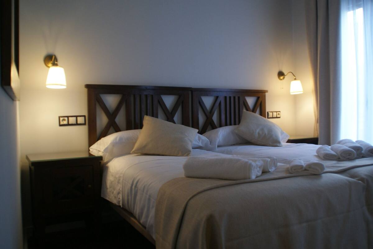 A hotel room with a large bed, two bedside tables, and two wall-mounted lamps.