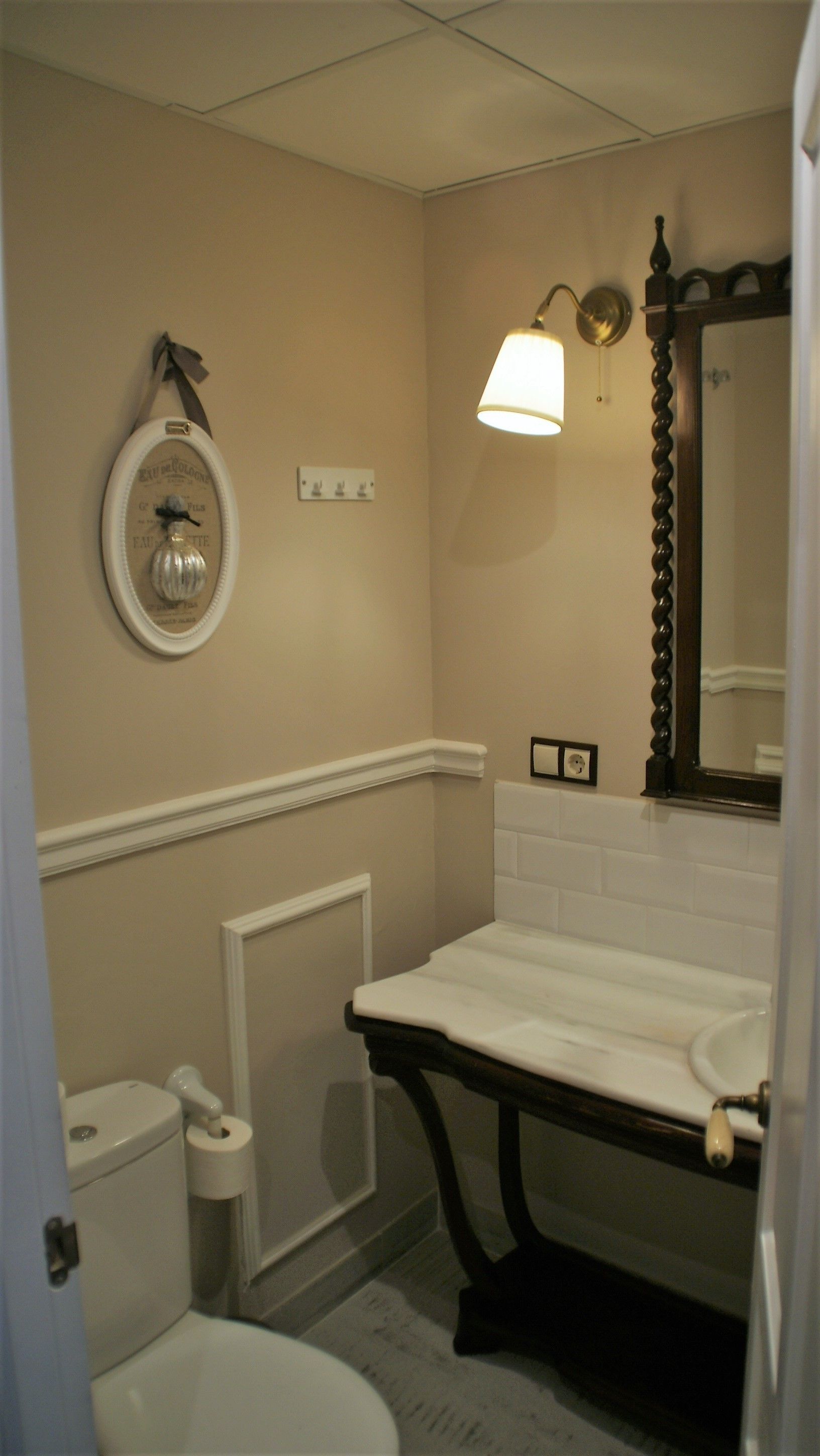 A bathroom with a toilet, sink, mirror, and wall-mounted light fixture.