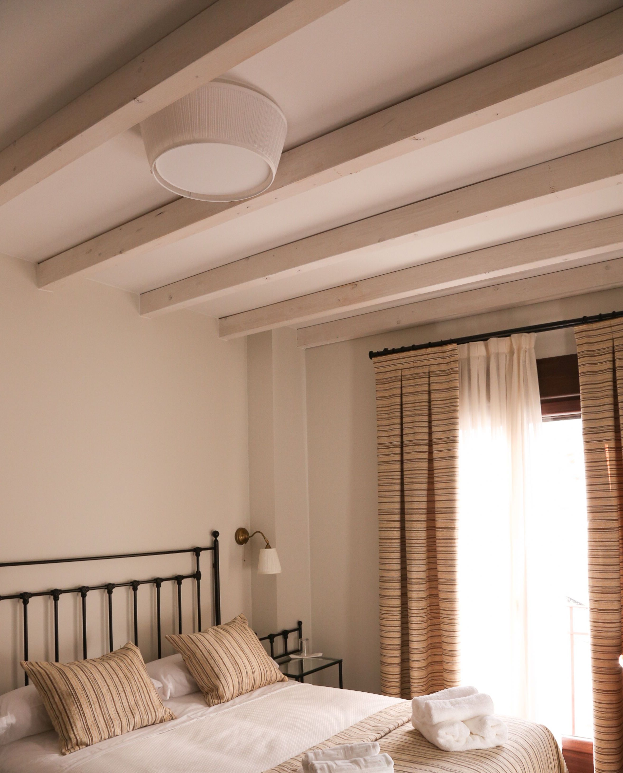 A bedroom with a bed, striped pillows, a bedside table with a lamp, and a window with curtains.