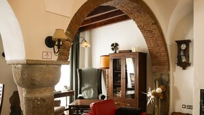 A room with a stone pillar, a red sofa, a wooden cabinet, and a table with a lace tablecloth. - Lantigua Casa Rural (Hinojosa del Duque)