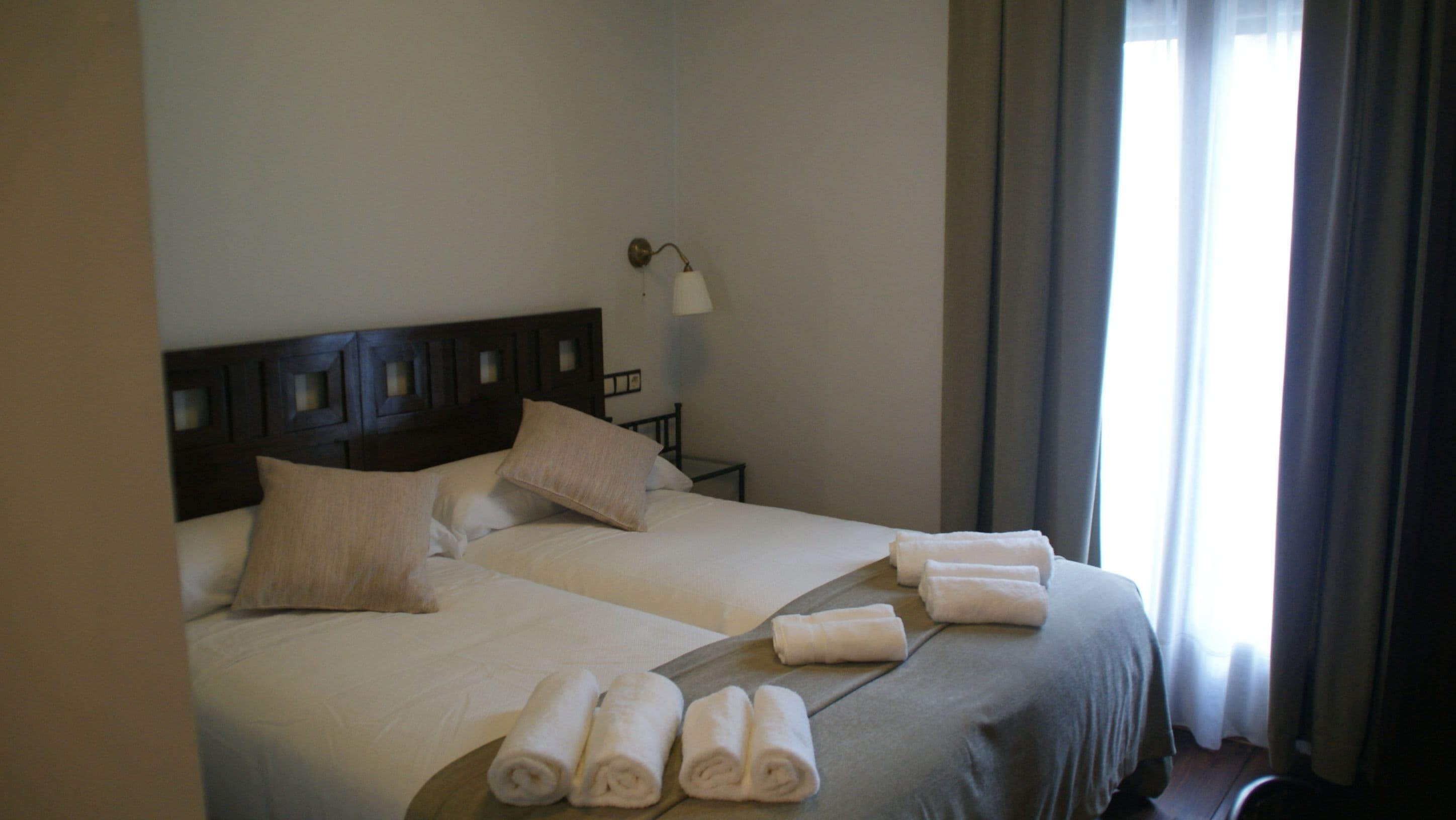 Een hotelkamer met twee bedden, een nachtkastje, een lamp en een raam met gordijnen.