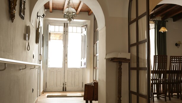 A hallway with a wooden floor, white doors, and a chandelier. There are chairs and a table in the background. - Lantigua Casa Rural (Hinojosa del Duque)