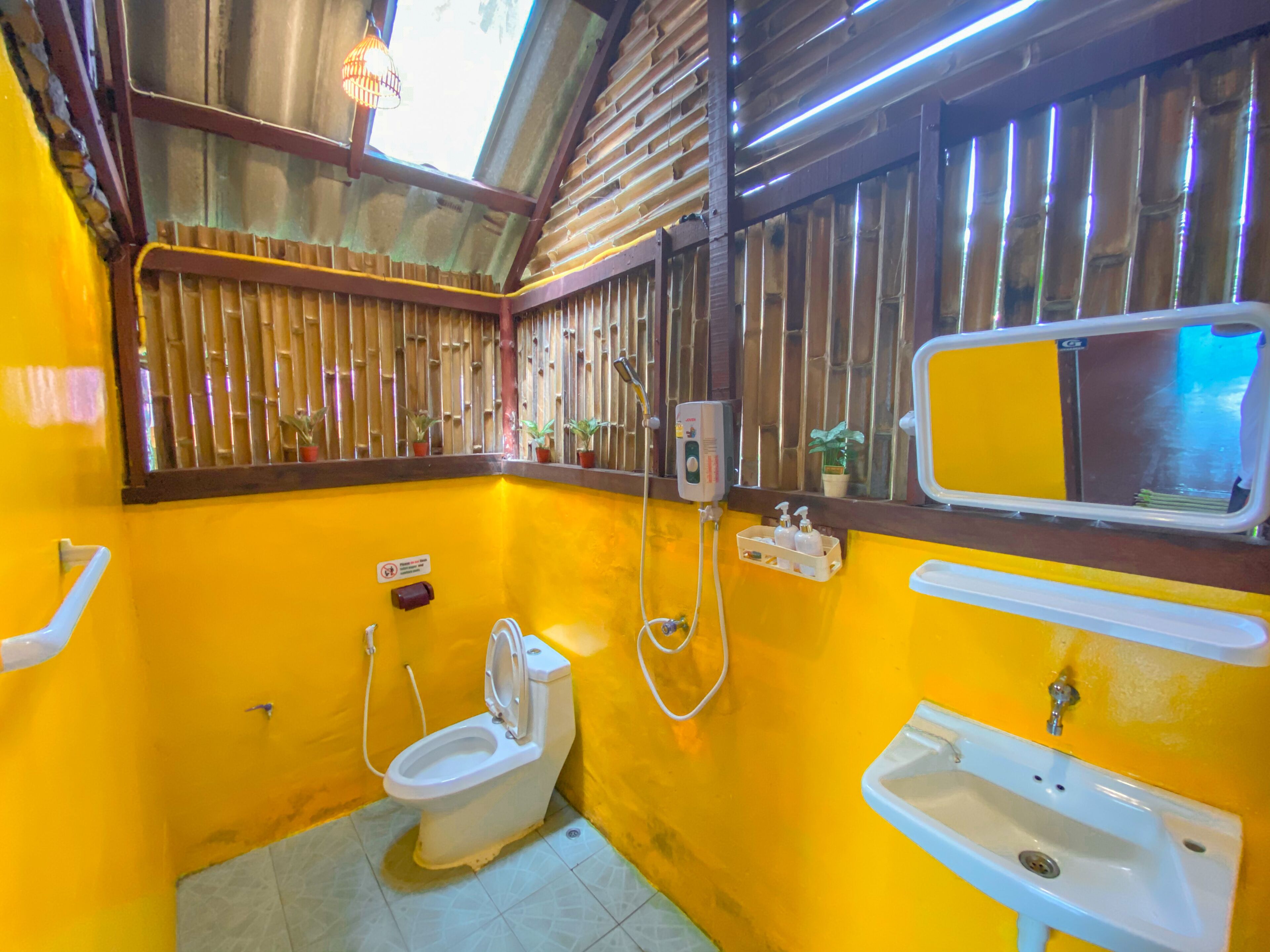 A bathroom with a yellow wall, a toilet, a sink, a mirror, and a shower.