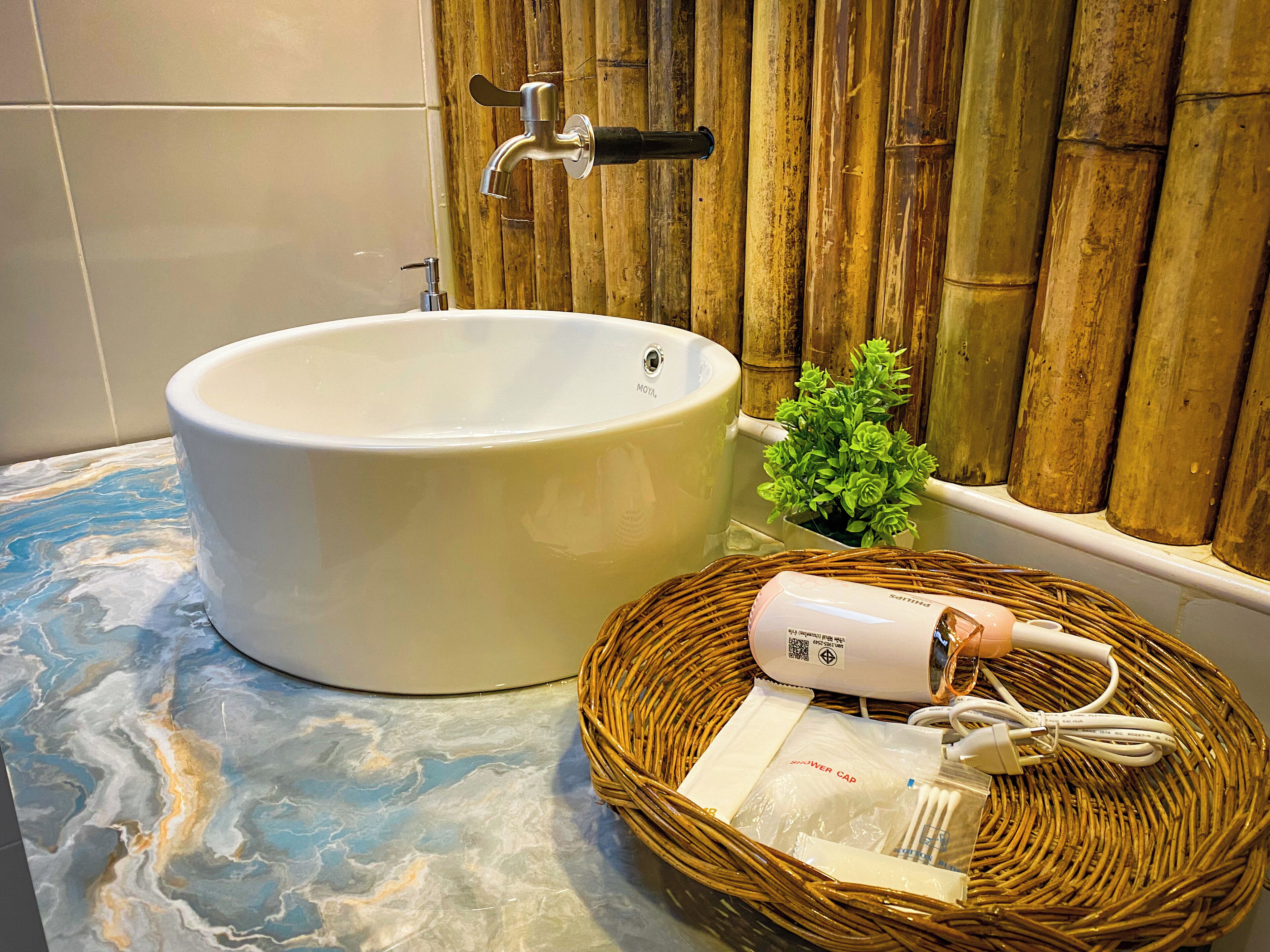 Une salle de bain avec une grande baignoire, une petite plante en pot et un panier en osier contenant des articles de toilette.