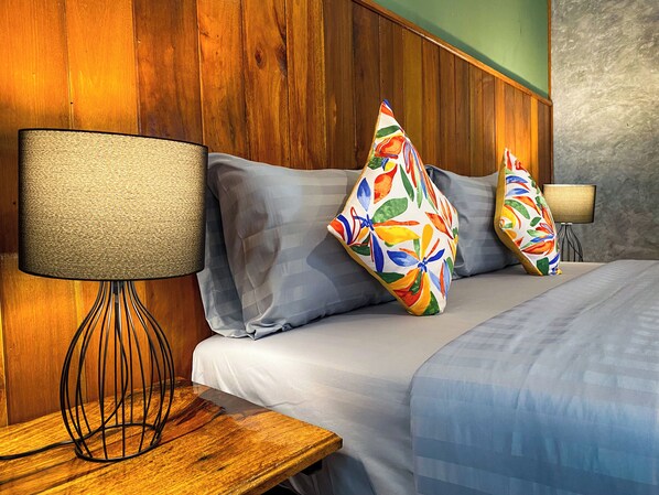 A hotel room with a wooden headboard, a bed with grey bedding, and colorful floral pillows.