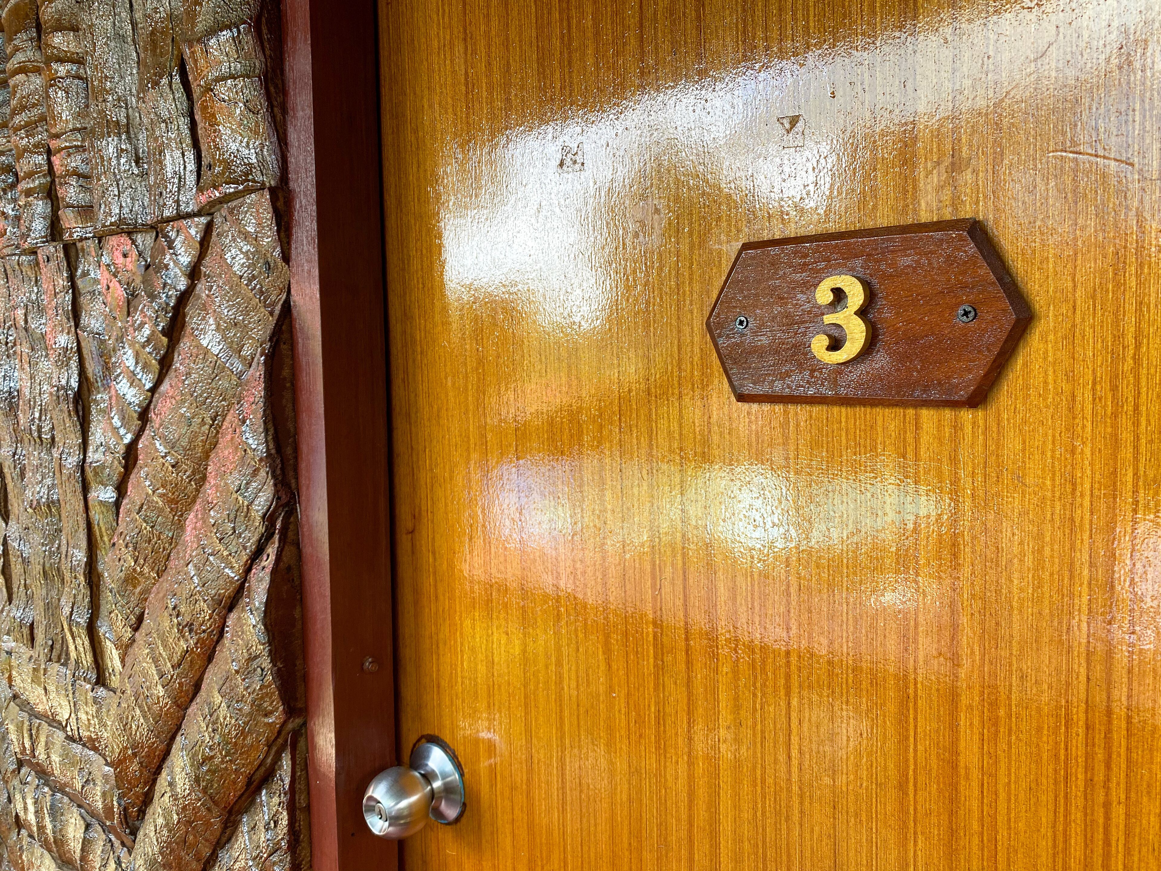 A wooden door with a brass doorknob and a brass plate with the number 3.