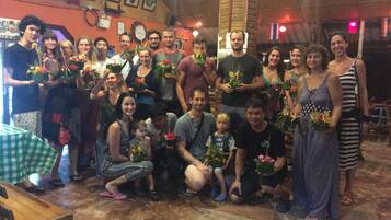 A group of people posing indoors with potted plants, a checkered table, and a brick wall with framed pictures.