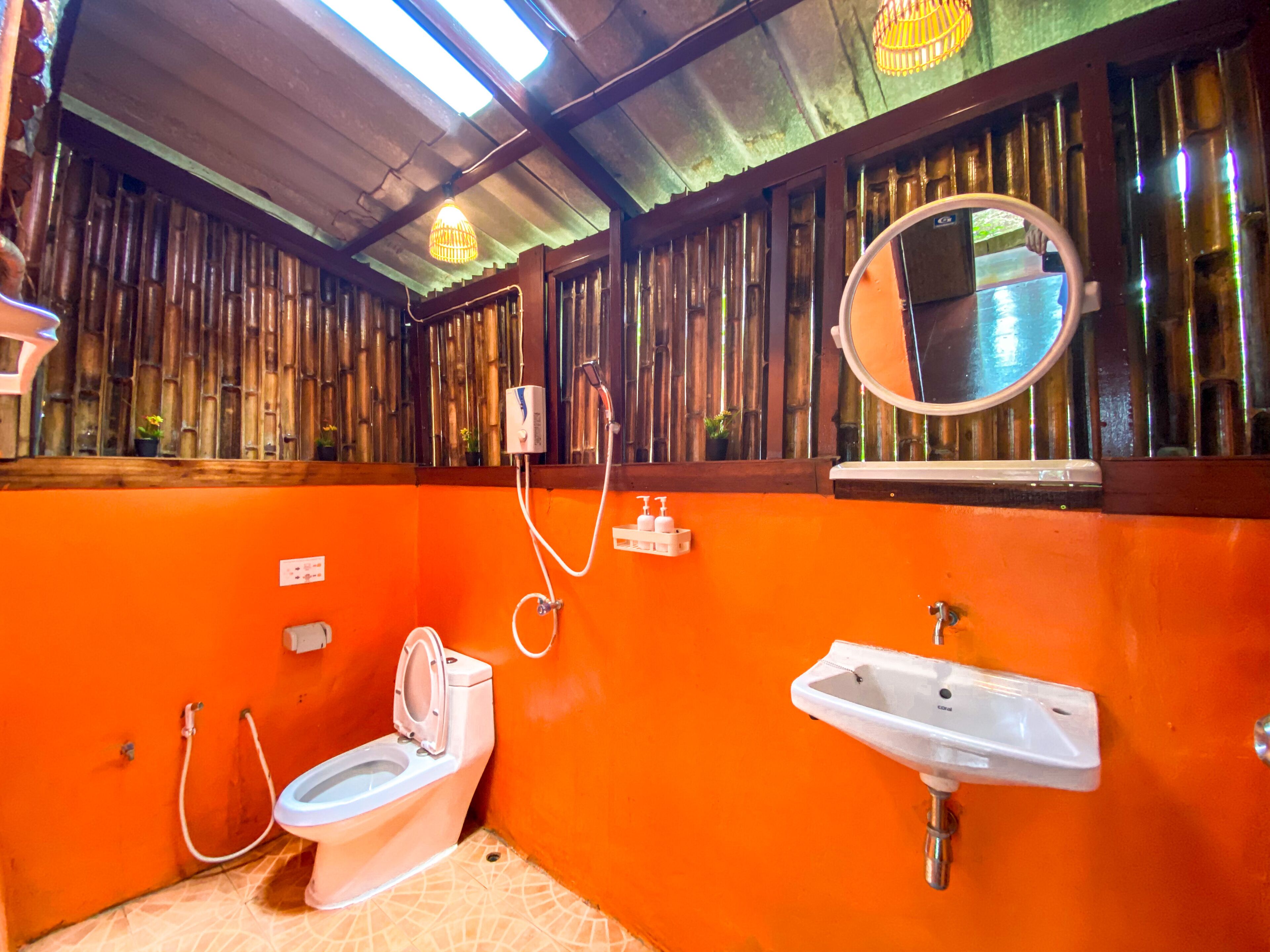 A bathroom with an orange wall, a toilet, a sink, a mirror, and a shower.