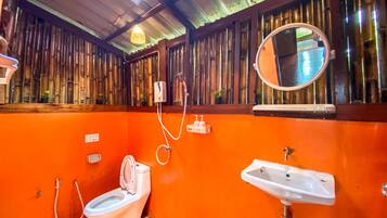 A bathroom with an orange wall, a toilet, a sink, a mirror, and a shower.