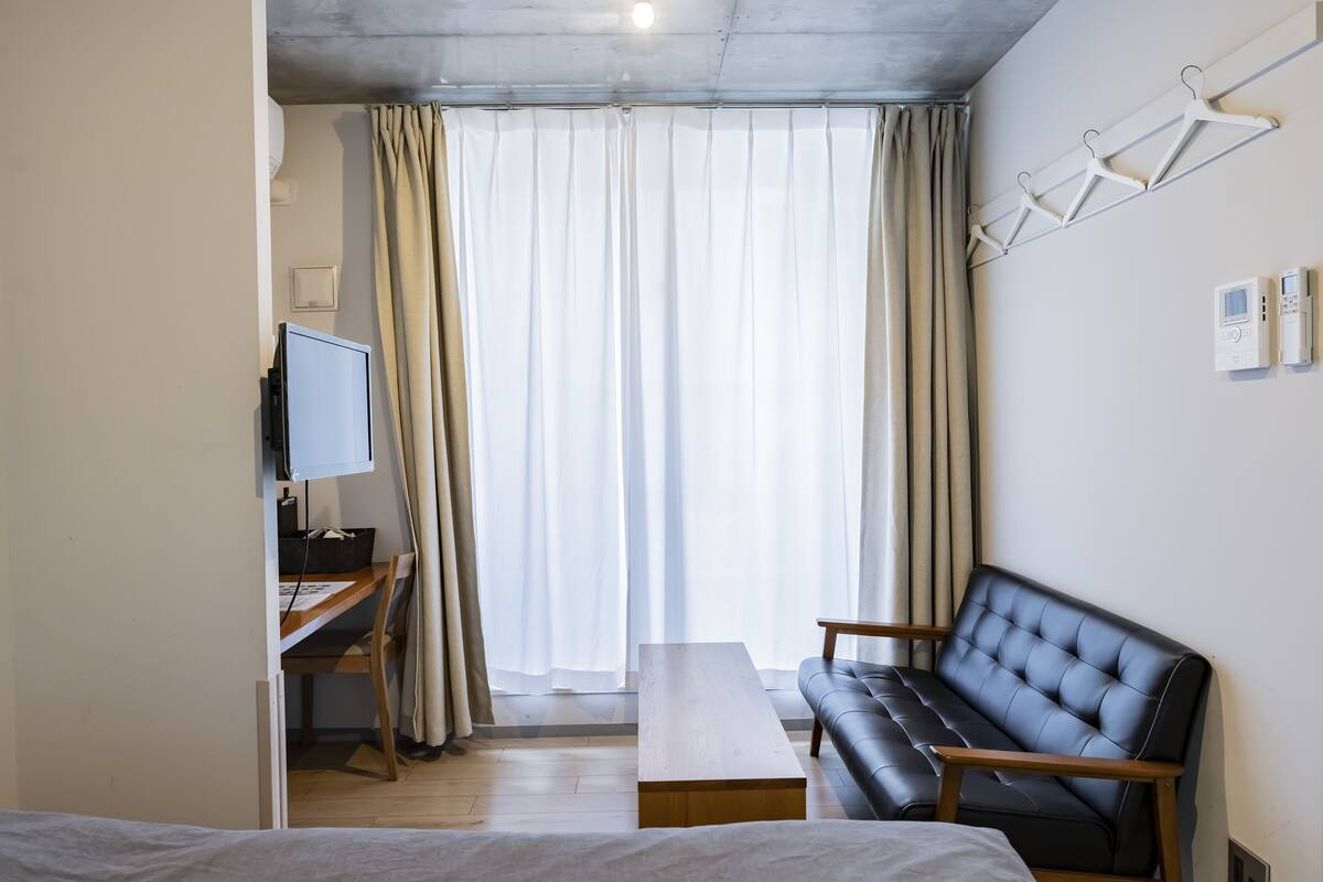A hotel room with a bed, a desk with a computer, a sofa, and a large window with curtains.