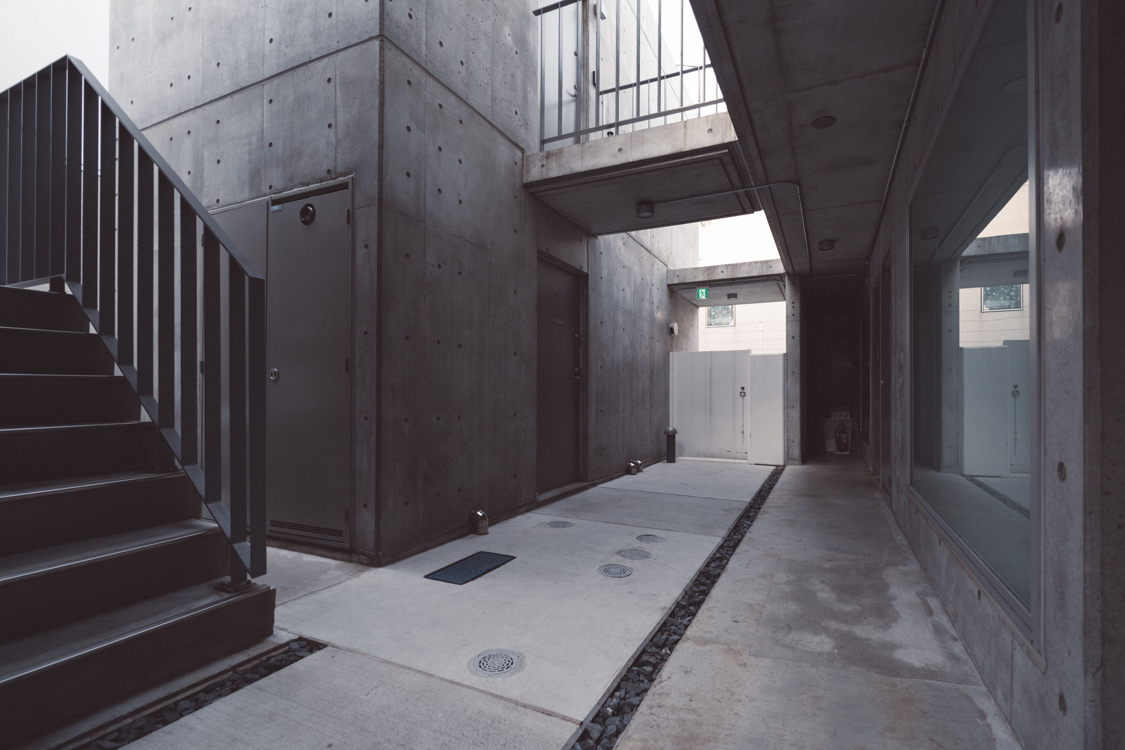 Un pasillo con una escalera, paredes de concreto y una ventana.