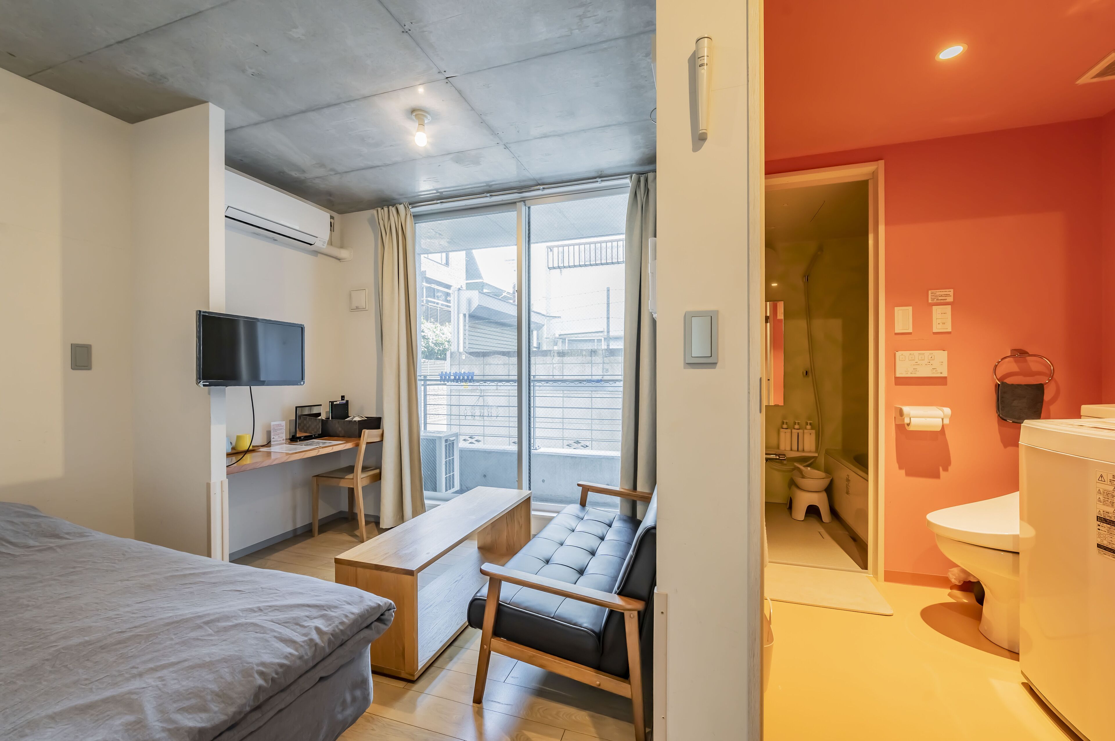 Habitación de hotel pequeña con cama, escritorio y silla, sofá, televisión y baño con inodoro y lavamanos.