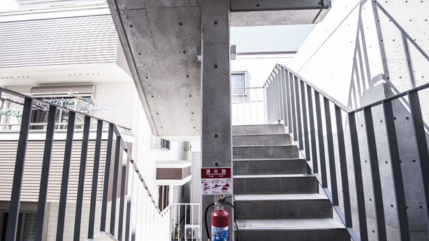 A fire extinguisher mounted on a concrete pillar in a stairwell with metal railings. - bmj Shinjuku Okubo (Tokyo)