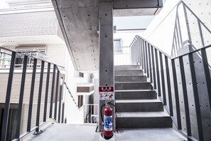 A fire extinguisher mounted on a concrete pillar in a stairwell with metal railings. - bmj Shinjuku Okubo (Tokyo)