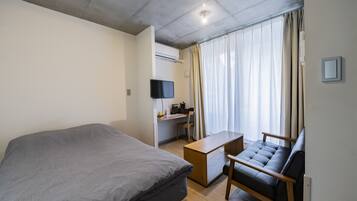 Moderni hotellihuone, jossa on suuri sänky, työpöytä tietokoneella, tuoli ja sohva.