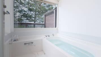 Un baño con bañera, inodoro y ventana con vistas a árboles.
