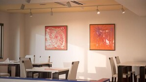 Une salle de conférence avec des tables et des chaises, deux tableaux abstraits accrochés au mur et des luminaires au plafond.