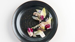 Une assiette noire sur laquelle sont disposés divers aliments, notamment des champignons, des fleurs et des feuilles.