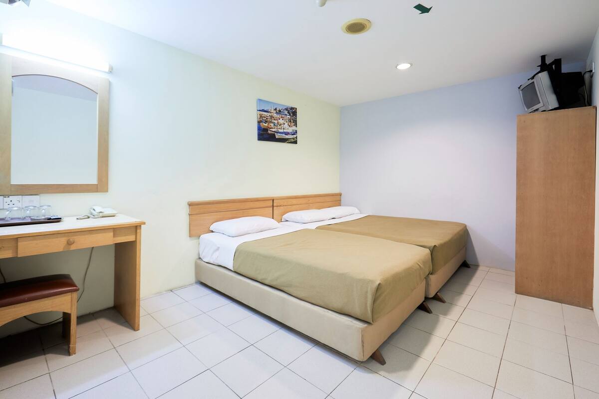 Une chambre d’hôtel avec un bureau en bois, deux lits, un miroir et un petit tableau accroché au mur.