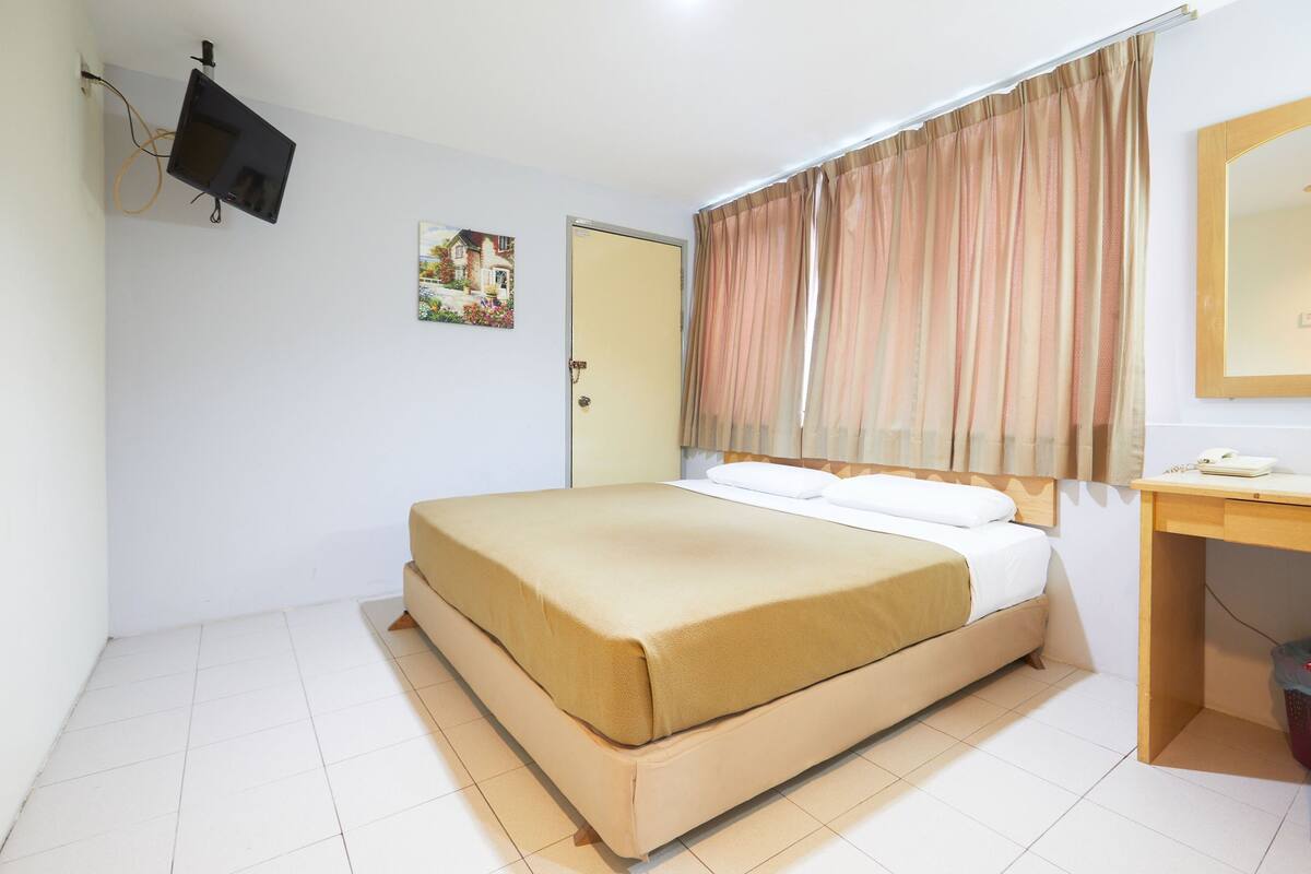 Une chambre à coucher avec un lit, un bureau, un téléviseur fixé au mur et une porte.