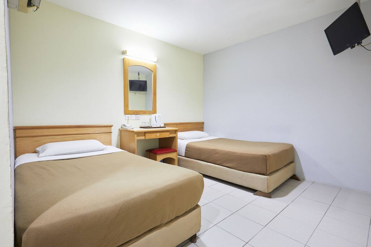 Une chambre d’hôtel avec deux lits, un bureau avec un miroir et un petit tabouret.
