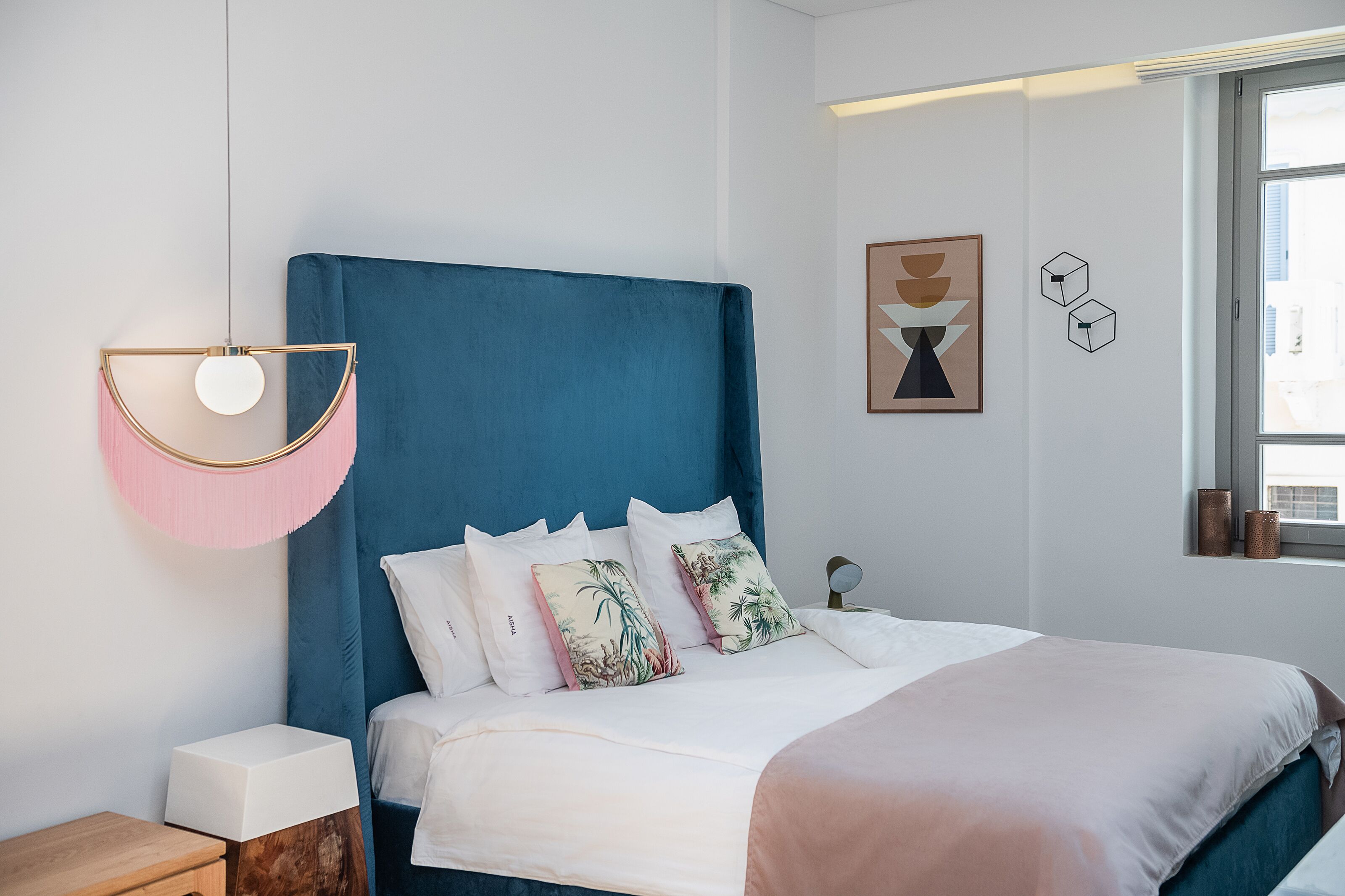Een moderne slaapkamer met een groot bed, nachtkastje, hanglamp en een raam met uitzicht.