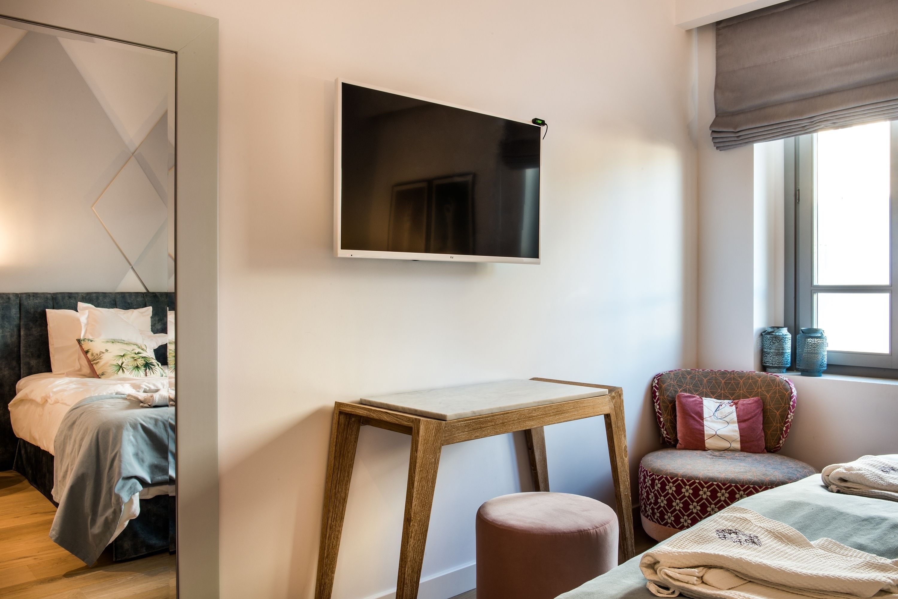 Ein modernes Schlafzimmer mit einem Bett, einem Nachttisch aus Holz, einem kleinen Hocker und einem an der Wand befestigten Fernseher.